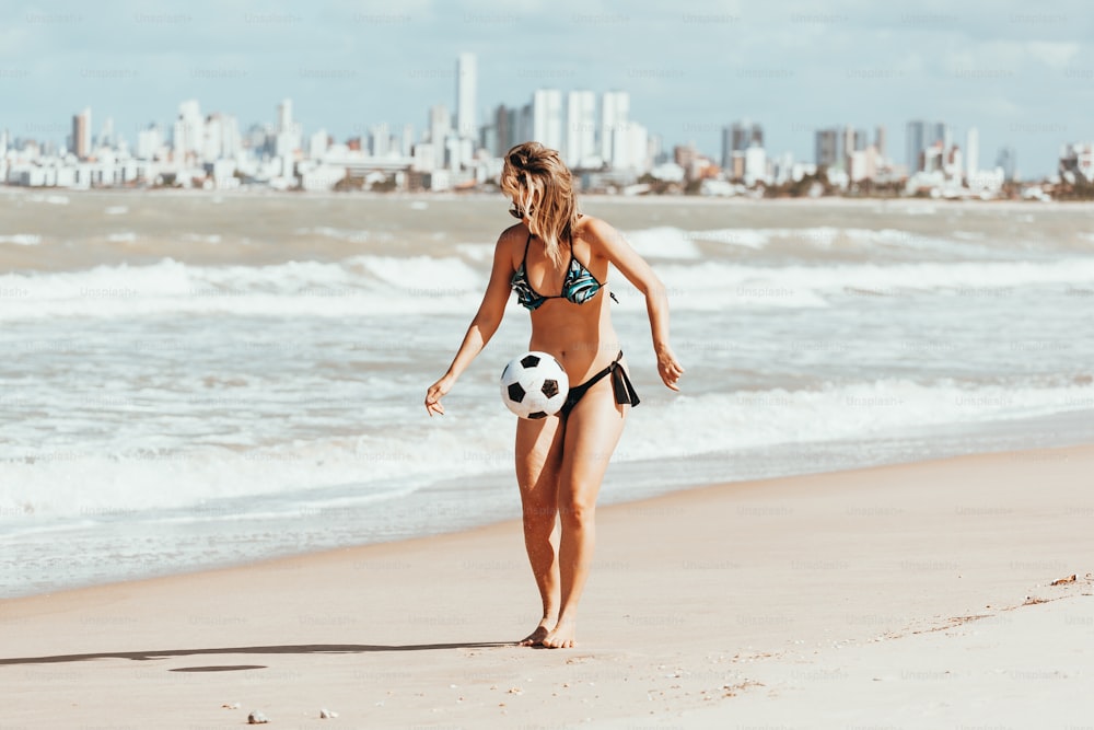 Mujer joven jugando al fútbol en la playa
