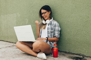 Portrait of young woman using laptop with headphones on the street