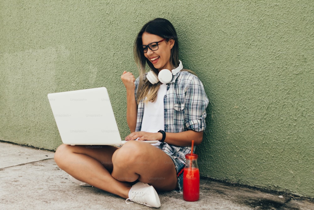 Retrato de una mujer joven usando una computadora portátil con auriculares en la calle