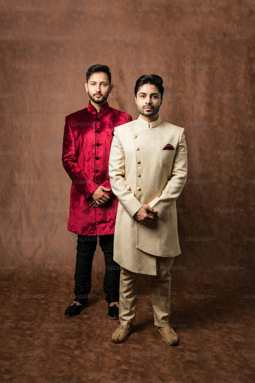 zwei indische Männer tragen ethnische oder traditionelle Kleidung, männliche Models mit Sherwani- oder Kurta-Pyjama, stehen und posieren über braunem Grunge-Hintergrund, selektiver Fokus