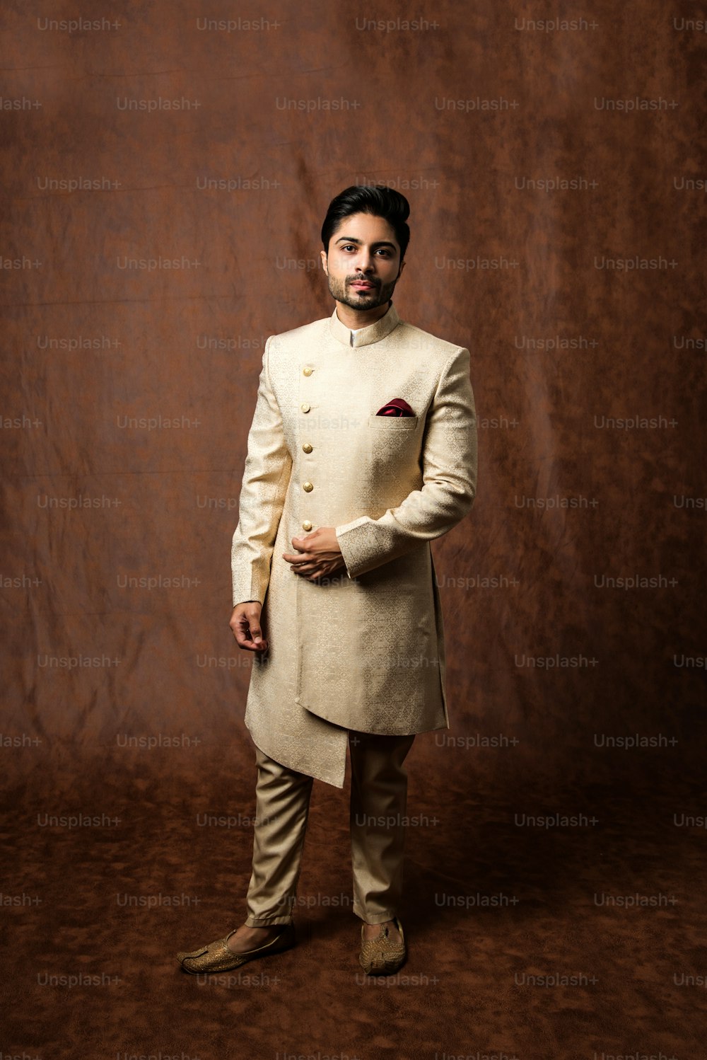 El novio indio usa kurta / telas étnicas o tradicionales.  Modelo masculino en sherwani, posando / de pie contra fondo grunge marrón, enfoque selectivo