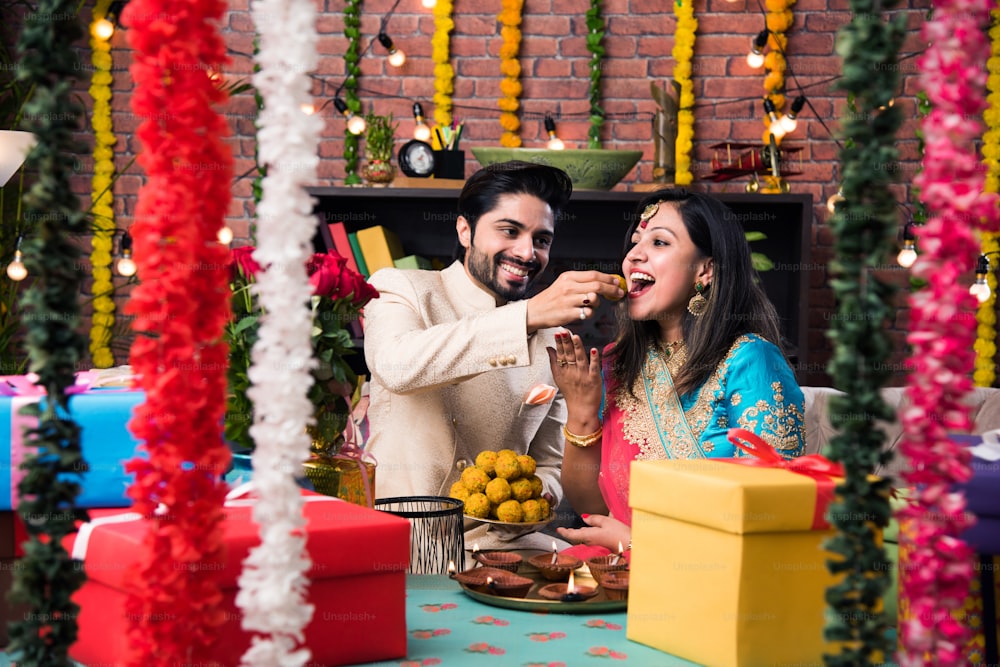 Casal inteligente indiano comendo laddu doce no Diwali ou aniversário, foco seletivo