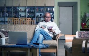 homem indiano / asiático sênior contabilidade com dinheiro, laptop e calculadora em casa
