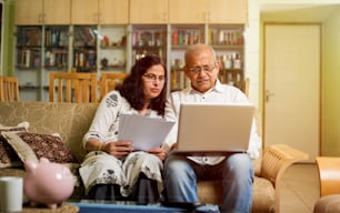 Comptabilité de couple indien / asiatique senior, faire du financement de la maison et vérifier les factures avec un ordinateur portable, une calculatrice et de l’argent tout en étant assis dans le jardin de la maison