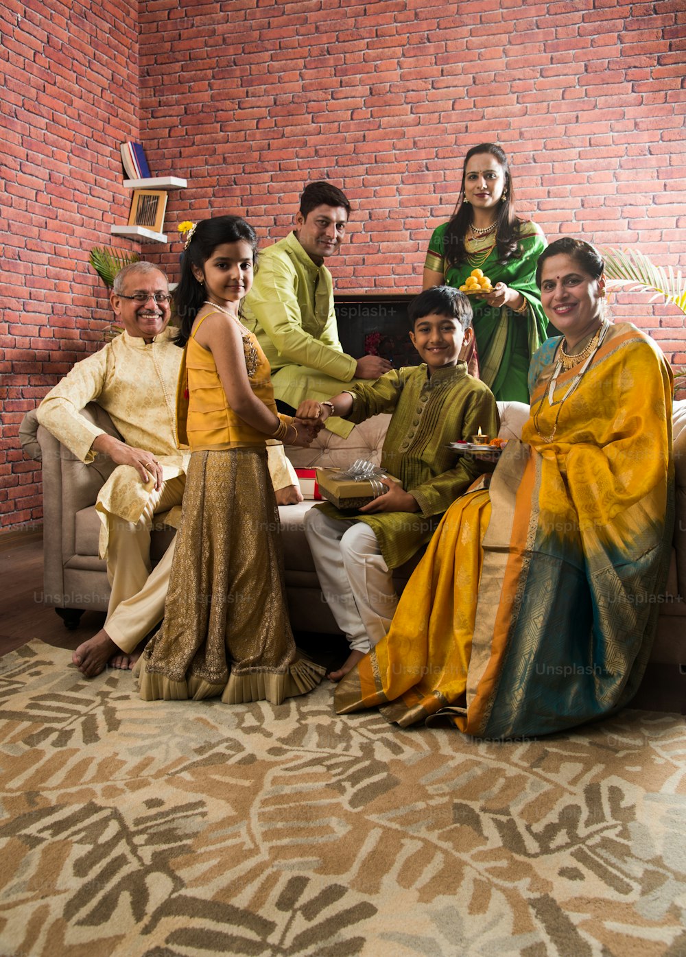 ラクシャバンダンまたはラクシャバンダンまたはラキ-ソファで両親と祖父母と一緒にラクシャバンダンを祝うインドの小さな兄弟姉妹
