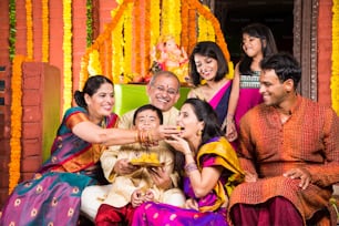 Foto di gruppo di allegra famiglia indiana che mangia dolci incontri o laddu sul festival di Ganesh, felice famiglia indiana e celebrazione del festival di Ganpati