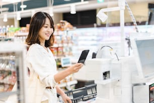 Mulher nova que usa o pagamento do smartphone em um supermercado