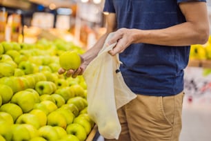 Man chooses apples in a supermarket without using a plastic bag. Reusable bag for buying vegetables. Zero waste concept.