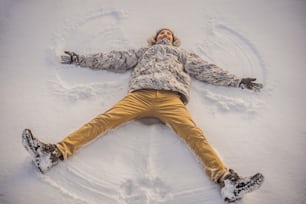 a young man in jacket lies on the snow and makes the figure of an angel. Winter fun.