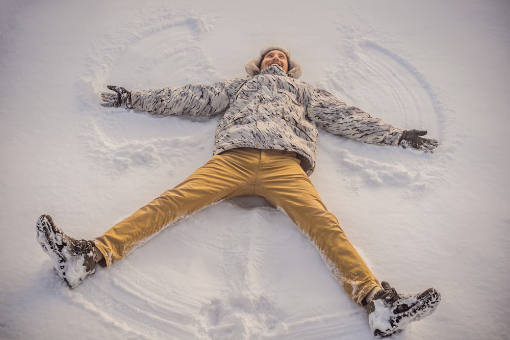 Un joven con chaqueta yace en la nieve y hace la figura de un ángel. Diversión invernal.