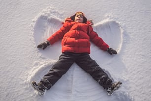 子供、男の子は雪の上に横たわり、腕と脚、感情、笑いで雪の天使を作ります。