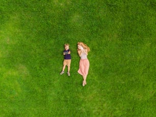 Mom and son are lying on the grass in the park. Mom looks at the phone, son looks at the tablet. Photos from the drone, quadracopter.