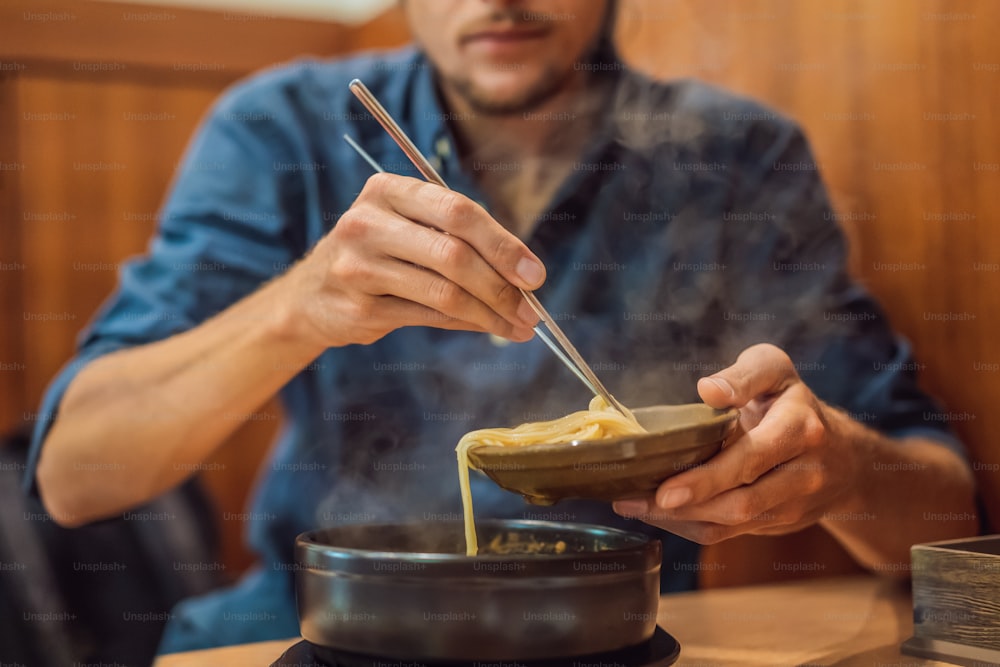 Male tourist eating Korean noodles in a Korean cafe. Travel Korea Concept.