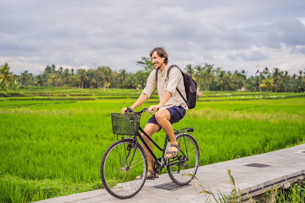 Ein junger Mann fährt mit dem Fahrrad auf einem Reisfeld in Ubud, Bali. Bali Reisekonzept.