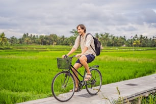 A young man rides a bicycle on a rice field in Ubud, Bali. Bali Travel Concept.