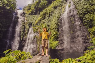 Menino bonito retrata o rei da selva contra o pano de fundo de uma cachoeira. Conceito de infância sem gadgets. Conceito de viajar com crianças. Conceito de infância ao ar livre.
