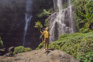 Menino bonito retrata o rei da selva contra o pano de fundo de uma cachoeira. Conceito de infância sem gadgets. Conceito de viajar com crianças. Conceito de infância ao ar livre.