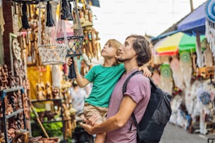 Dad and son at a market in Ubud, Bali. Typical souvenir shop selling souvenirs and handicrafts of Bali at the famous Ubud Market, Indonesia. Balinese market. Souvenirs of wood and crafts of local.