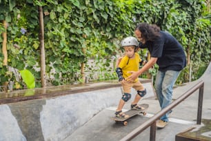 Athletic boy learns to skateboard with a trainer in a skate park. Children education, sports.