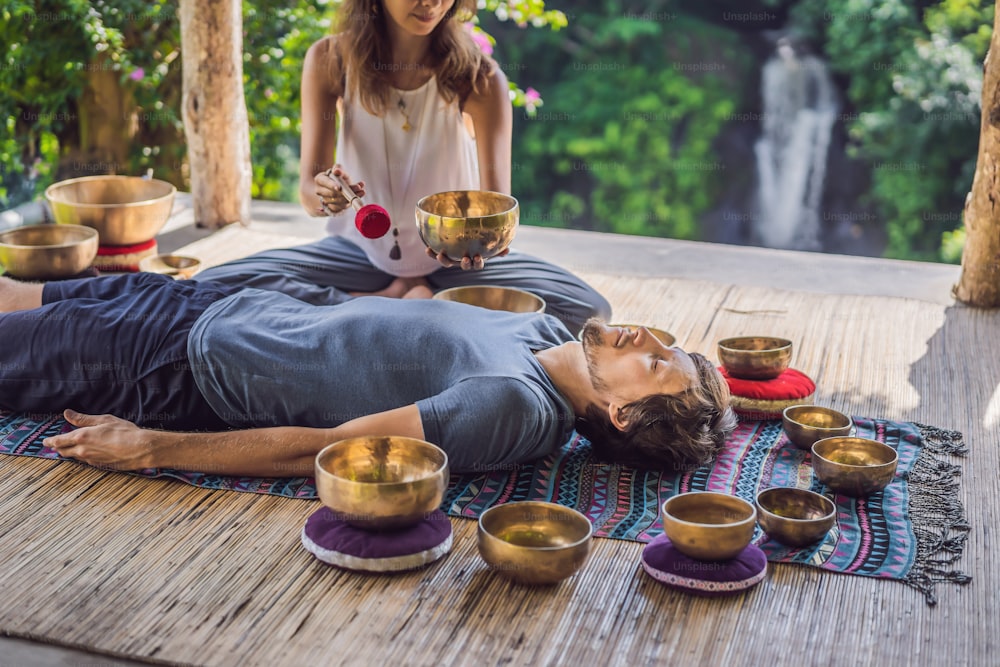 Nepal Buddha copper singing bowl at spa salon. Young beautiful man doing massage therapy singing bowls in the Spa against a waterfall. Sound therapy, recreation, meditation, healthy lifestyle and body care concept.