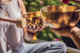 Nepal Buddha copper singing bowl at spa salon. Young beautiful woman doing massage therapy singing bowls in the Spa against a waterfall. Sound therapy, recreation, meditation, healthy lifestyle and body care concept.