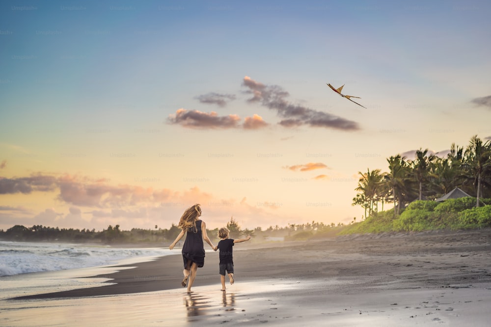 Maman et son fils courent sur la plage de la mer en lançant un cerf-volant.