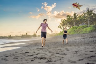 Young father and his son running with kite on the beach.
