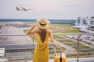 Beginn ihrer Reise. Schöne junge Frau in einem gelben Kleid und einem gelben Koffer wartet auf ihren Flug.