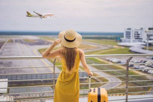 Start of her journey. Beautiful young woman ltraveler in a yellow dress and a yellow suitcase is waiting for her flight.