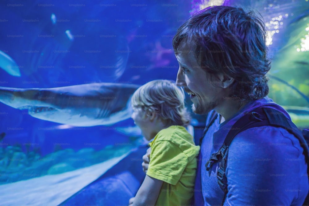 Père et fils regardant des poissons dans un aquarium tunnel.