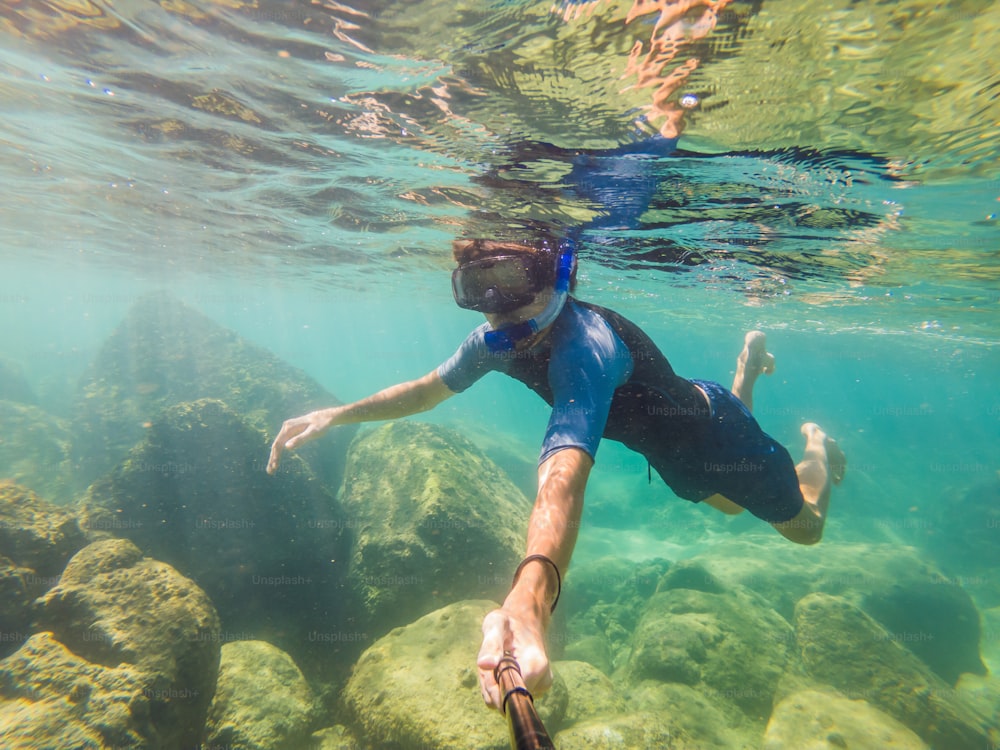 カラフルな魚と海洋生物を持つ深い青い海の水中サンゴ礁の風景背景を探索する若い男性。