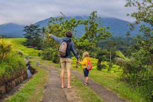 Vater und Sohn Reisende auf wunderschönen Jatiluwih-Reisterrassen vor dem Hintergrund berühmter Vulkane in Bali, Indonesien. Konzept des Reisens mit Kindern.