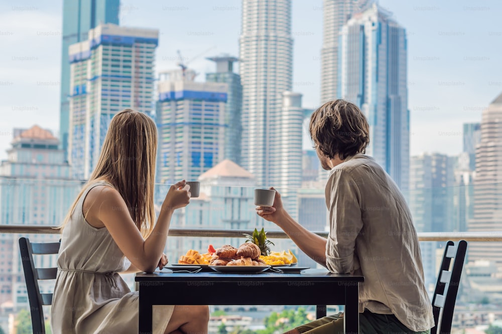 Loving couple having breakfast on the balcony. Breakfast table with coffee fruit and bread croisant on a balcony against the backdrop of the big city.
