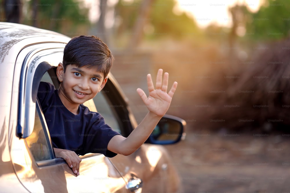Nettes indisches Kind, das aus dem Autofenster winkt