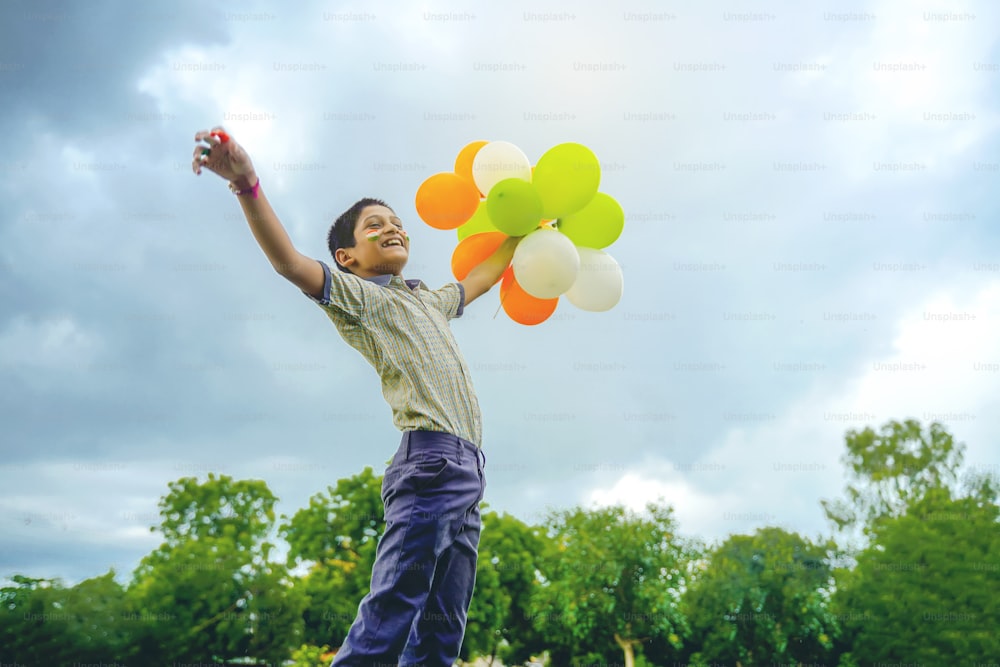 Pequeño escolar indio Saltando en el cielo con globos tricolores y celebrando el Día de la Independencia o la República de la India
