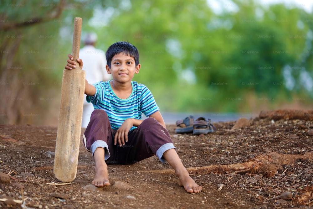 Bambino indiano rurale che si siede sul terreno con il pipistrello