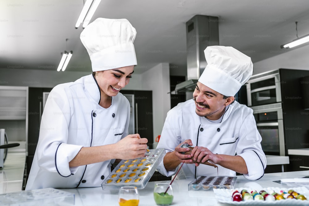 Joven pareja latina mujer y hombre chocolatero en uniforme de chef y sombrero preparando chocolates mexicanos dulces de bombón en la cocina en México América Latina