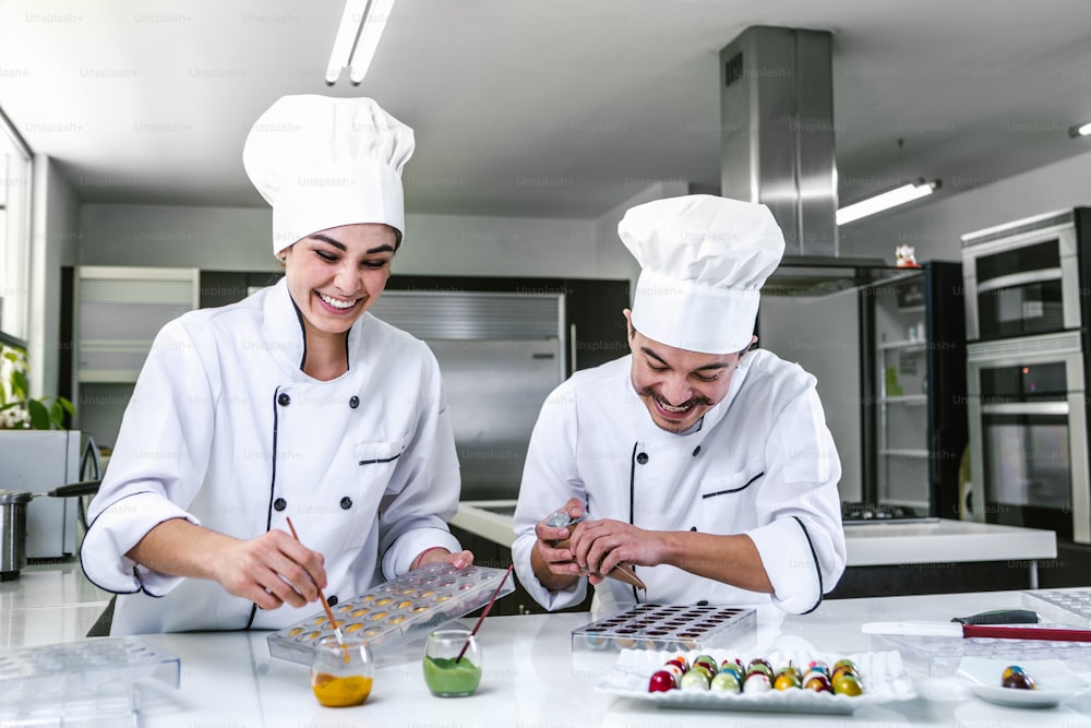 young latin couple woman and man chocolatier in chef uniform and hat preparing mexican chocolates bonbon candies at kitchen in Mexico Latin America
