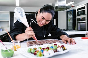 라틴 여성 페이스트리 셰프는 멕시코 라틴 아메리카의 주방에서 맛있는 과자 초콜릿을 준비하는 과정에서 검은색 유니폼을 입고 있다