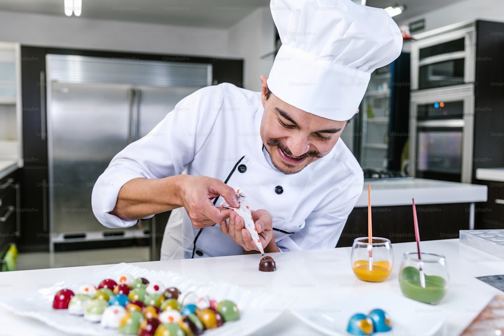 homem latino chef confeiteiro vestindo uniforme no processo de preparação de deliciosos chocolates doces na cozinha no México América Latina