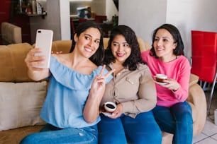 Latin women friends taking a selfie photo and drinking coffee in home in Mexico city