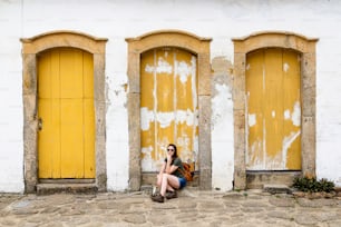 Beautiful model sitting on yellow door in historic city of Paraty, Rio de Janeiro, Brazil.