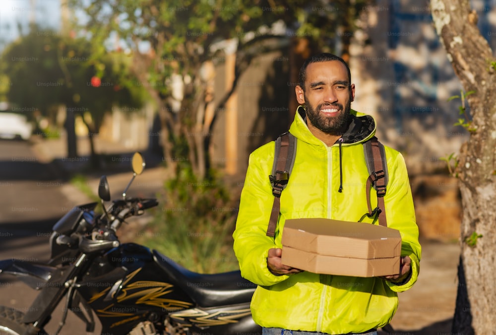 Motoboy afroamericano con scatole di pizza per la consegna.