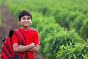 Mignon enfant indien avec sac sac dans un champ agricole