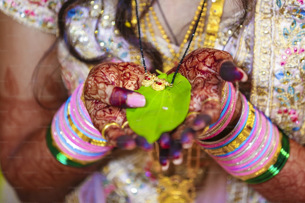 Novio indio y nupcial sosteniendo mangalsutra o collar de oro con hoja verde en la mano