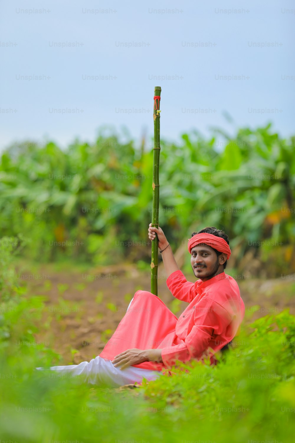 Joven agricultor indio vestido de tradicional y sosteniendo palo de madera en la mano en el campo
