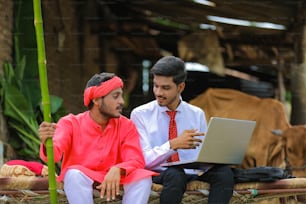 Young Indian agronomist showing some information to farmer in laptop at home