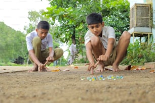 Indisches Kind, das mit Glasmurmeln spielt, was ein altes indisches Dorfspiel ist. Glasmurmeln werden in der Hindi-Sprache auch als Kancha bezeichnet.