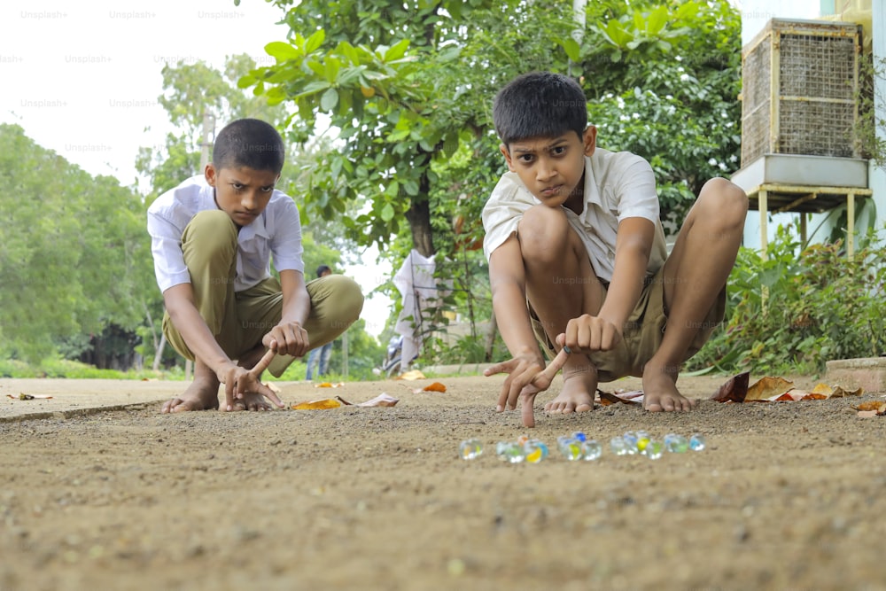 古いインドの村のゲームであるガラスのビー玉で遊ぶインドの子供。ガラスビー玉はヒンディー語でカンチャとも呼ばれます。