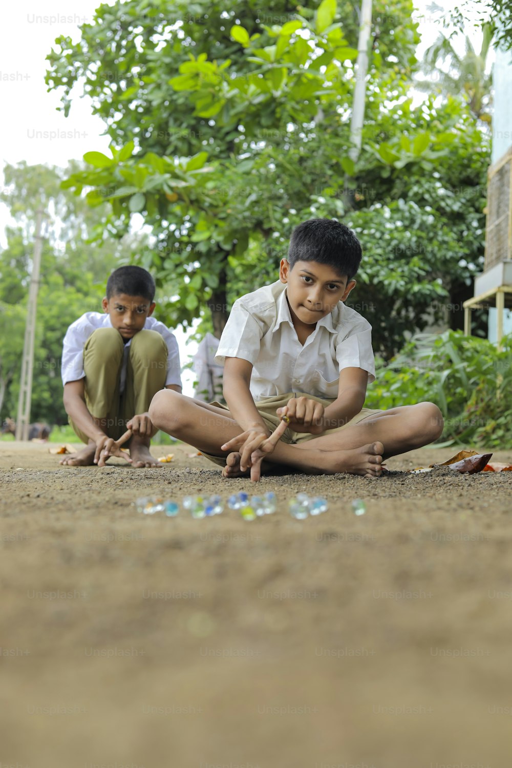 古いインドの村のゲームであるガラスのビー玉で遊ぶインドの子供。ガラスビー玉はヒンディー語でカンチャとも呼ばれます。